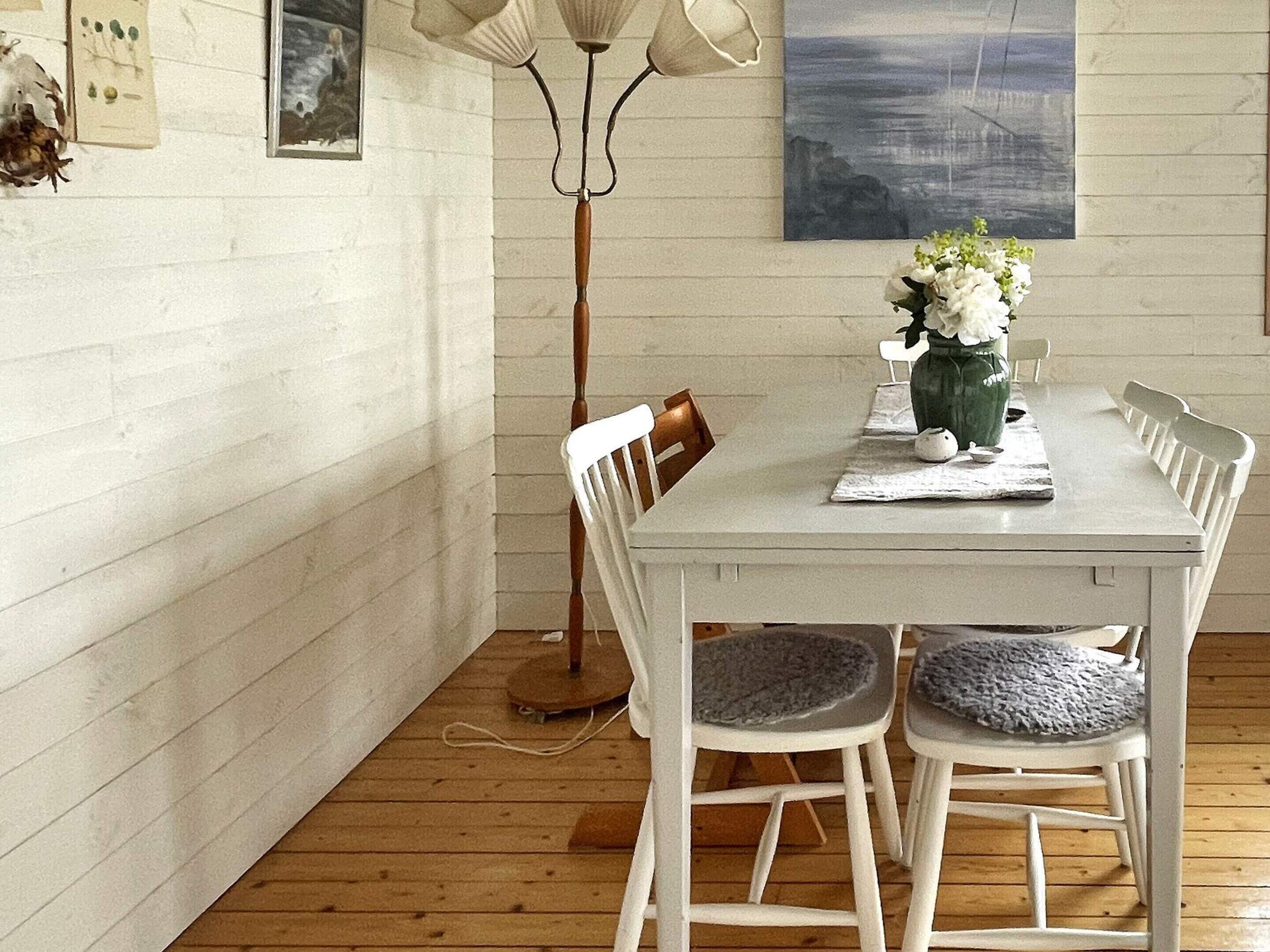 A dining area with a white table, chairs, a floor lamp, and a vase with flowers.