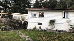 A white house with a stone pathway leading to a wooden deck, surrounded by a stone wall and greenery. - 4 Star Holiday Home in Uddevalla (Uddevalla)