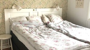 Un lit avec une literie à motifs floraux, une table de chevet blanche et un mur recouvert d’un papier peint à fleurs.