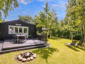Un patio moderno al aire libre con un hogar, una zona de estar y una terraza que conduce a una casa con un letrero visible.