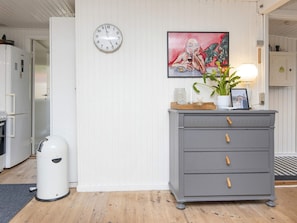 A kitchen with a white wall, a clock, a grey cabinet, and a painting.