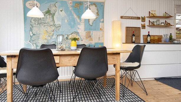 A dining area with a wooden table, black chairs, a black and white patterned rug, and a large map on the wall. - 5 Person Holiday Home in Thyholm (Thyholm)