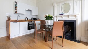 A modern kitchen with white cabinetry, a wooden countertop, and a dining area with a glass table and brown chairs. - Pembridge Villas VI by onefinestay (London)