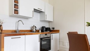 A compact kitchen with white cabinets, a stainless steel sink, a coffee maker, and an oven. - Pembridge Villas VI by onefinestay (London)