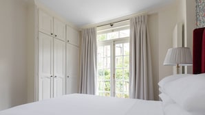 A bedroom with a large bed, a window with curtains, a wardrobe, and a lamp. - Pembridge Villas VI by onefinestay (London)