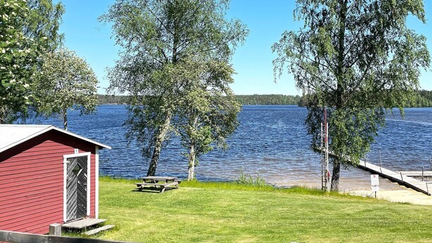 A lakeside view with a red cabin, picnic table, and wooden dock. - 5 Person Holiday Home in Ydre (Österbymo)