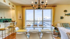 A modern living room with a glass dining table, white chairs, a sofa, and a large window with curtains. - Stunning Gulf front condo, shorter stays welcomed, great rates. (DESTIN)