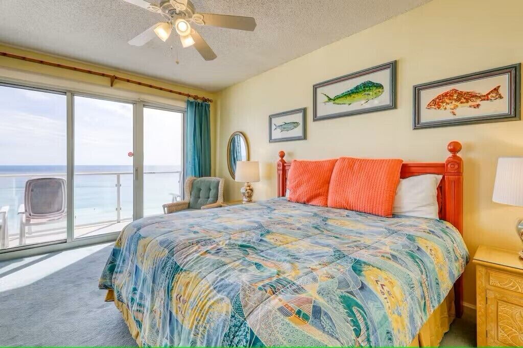 Ein Schlafzimmer mit einem großen Bett, einem Deckenventilator und Blick auf das Meer durch eine Schiebetür.