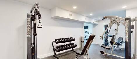 A gym with weightlifting equipment, a bench, and a rack of dumbbells.