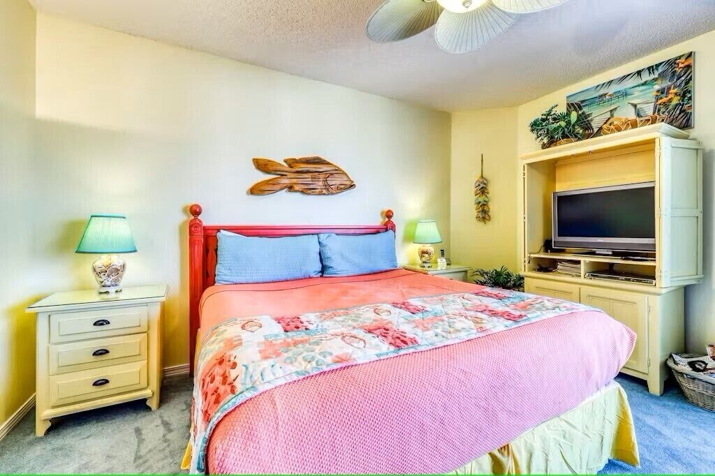 Un dormitorio con una cama, dos mesitas de noche, un televisor y un estante en la pared.
