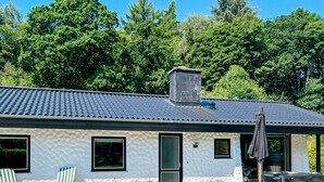 Une maison moderne avec un toit en tuiles, un patio couvert avec des meubles d’extérieur et un jardin.