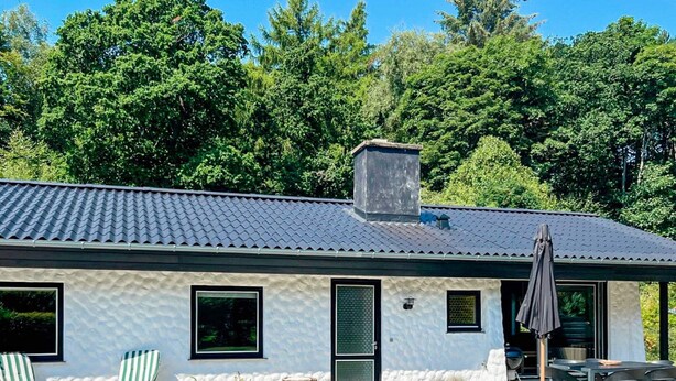 Ein modernes Haus mit Ziegeldach, einer überdachten Terrasse mit Gartenmöbeln und einem Garten.