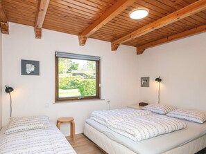 A bedroom with two beds, a window, and wooden beams on the ceiling.