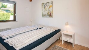 Ein Schlafzimmer mit einem Bett, einem Nachttisch, einer Lampe, einem Fenster und einem Bild an der Wand.