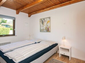 A bedroom with a bed, a nightstand, a lamp, a window, and a painting on the wall. - 7 Person Holiday Home in Ebeltoft (Ebeltoft)