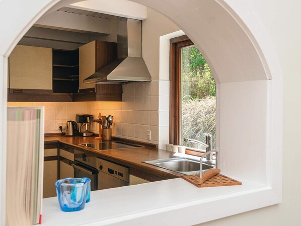 A modern kitchen with a built-in oven, a coffee maker, and a window overlooking greenery.