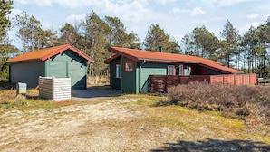 A rustic cabin with a green exterior and red roof, surrounded by trees and a gravel path. - 4 Person Holiday Home in Thisted (Thisted)