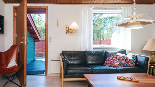 A cozy living room with a black leather sofa, a wooden coffee table, and a red chair. - 4 Person Holiday Home in Thisted (Thisted)