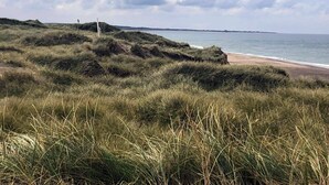 A coastal landscape with grassy dunes, a beach, and a body of water under a cloudy sky. - 4 Person Holiday Home in Thisted (Thisted)
