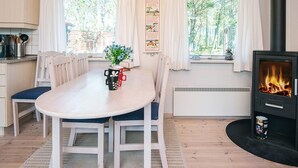 A cozy room with a wooden table, chairs, a fireplace, and large windows with curtains. - 4 Person Holiday Home in Thisted (Thisted)