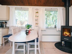 A cozy room with a wooden table, chairs, a fireplace, and large windows with curtains. - 4 Person Holiday Home in Thisted (Thisted)