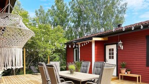 En træterrasse med et bord og stole, en rød bygning med en dør, og en hængende lampe.