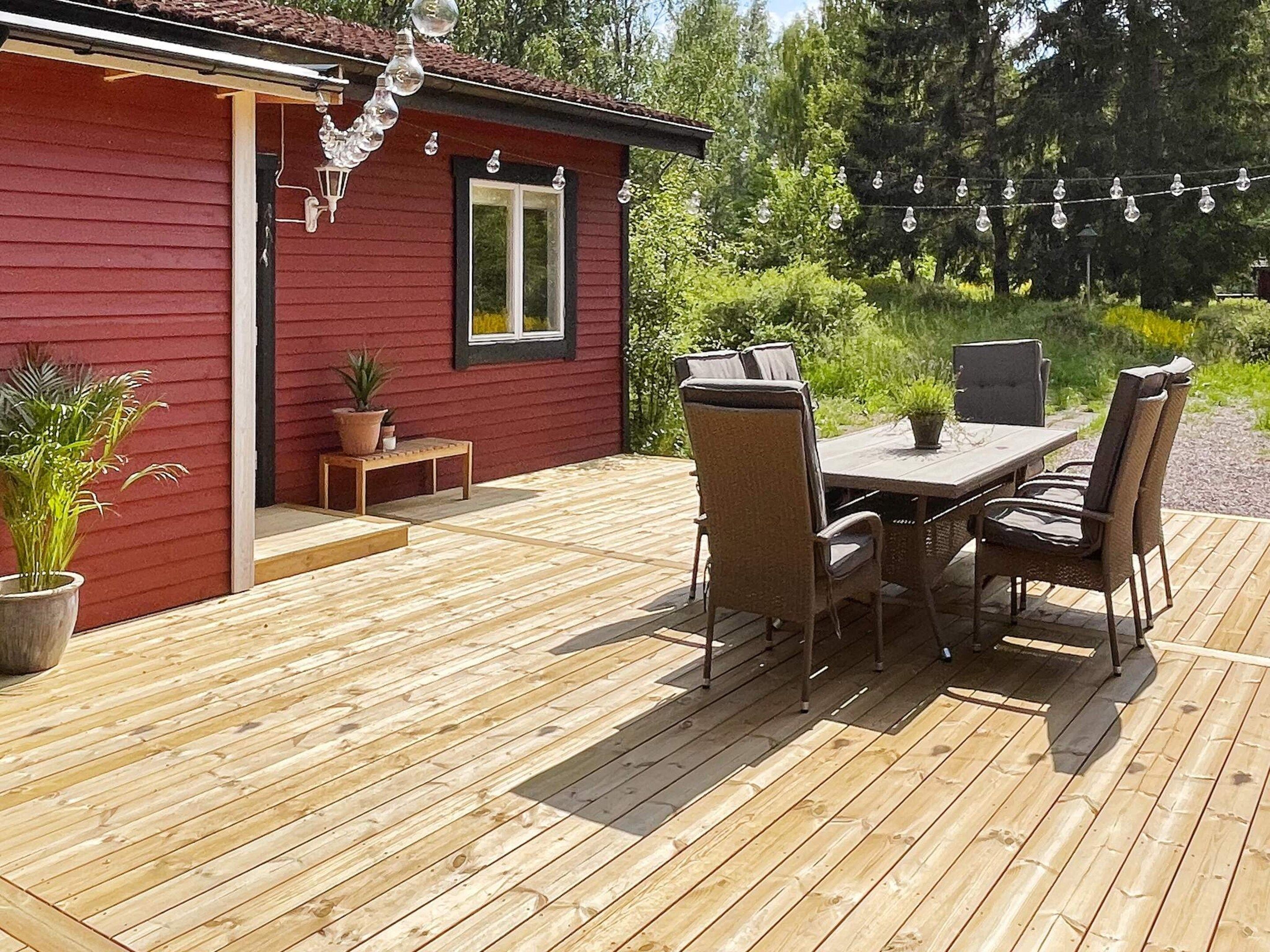 A wooden deck with a red building, outdoor furniture, and string lights.