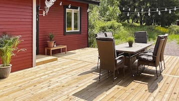 A wooden deck with a red building, outdoor furniture, and string lights.