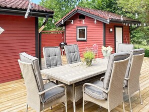 A red wooden house with a deck, a dining table with chairs, and a small garden area. - 4 Star Holiday Home in Edsbruk (Edsbruk)