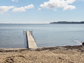 A wooden pier extending into calm water, a sandy beach, and a distant tree-covered landmass. - 4 Star Holiday Home in Hejls (Hejls)