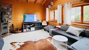 Interior acogedor de una cabaña con techo de madera, chimenea de piedra, televisor de pantalla plana, sofá y alfombra de cuero de vaca.