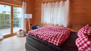 Un dormitorio de cabaña de madera con una cama, una silla, una lámpara y vistas a través de una puerta corrediza.