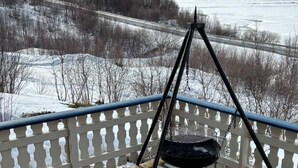 A balcony with a metal grill, overlooking a snowy landscape with a road and trees. - 7 Person Holiday Home in Tana (Tana)