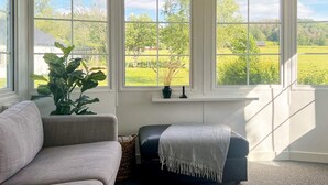 A room with a grey sofa, a black ottoman, and a large window with a view of a green landscape. - 3 Person Holiday Home in Huskvarna (Huskvarna)