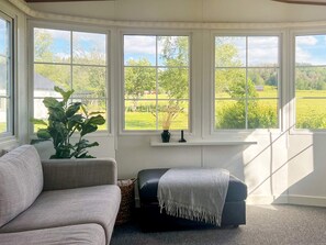 A room with a grey sofa, a black ottoman, and a large window with a view of a green landscape. - 3 Person Holiday Home in Huskvarna (Huskvarna)