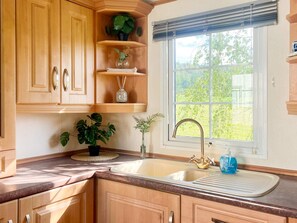 A kitchen with wooden cabinets, a sink, and a window with a view of greenery. - 3 Person Holiday Home in Huskvarna (Huskvarna)