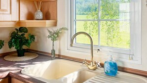 A kitchen with a double sink, wooden cabinets, a window with a view of greenery, and a potted plant on the counter. - 3 Person Holiday Home in Huskvarna (Huskvarna)