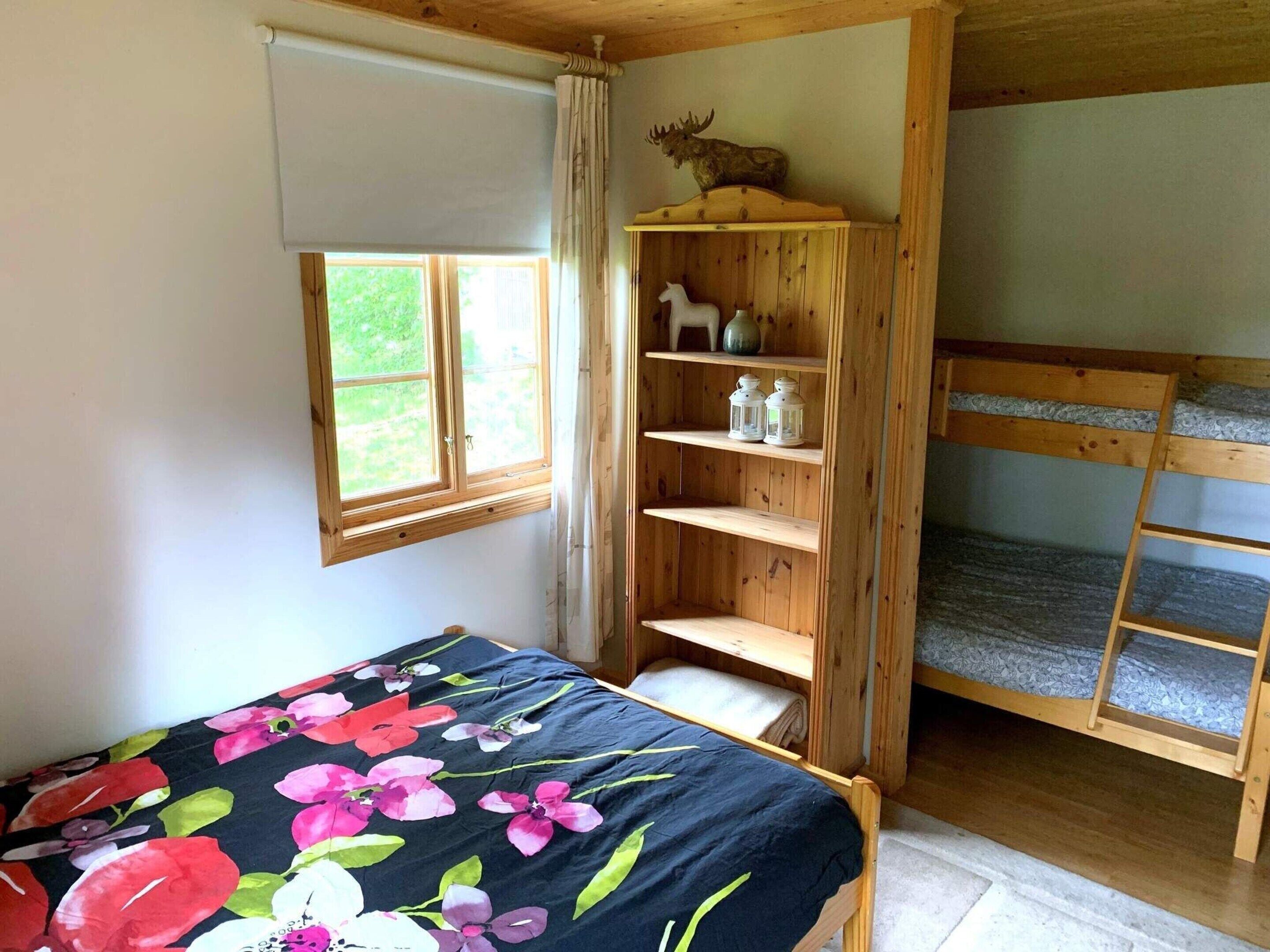 A room with a bed, a wooden shelf with decorative items, a window, and a bunk bed.