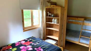 A room with a bed, a wooden shelf with decorative items, a window, and a bunk bed.