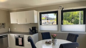 A modern kitchen with white cabinets, a built-in oven, and a dining area with a round table and chairs. - 6 Person Holiday Home in Bomlo (Bomlo)