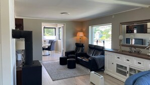 A modern living room with a sofa, a dining area with a table and chairs, a large window with a view, and a mirror above a cabinet. - 6 Person Holiday Home in Bomlo (Bomlo)