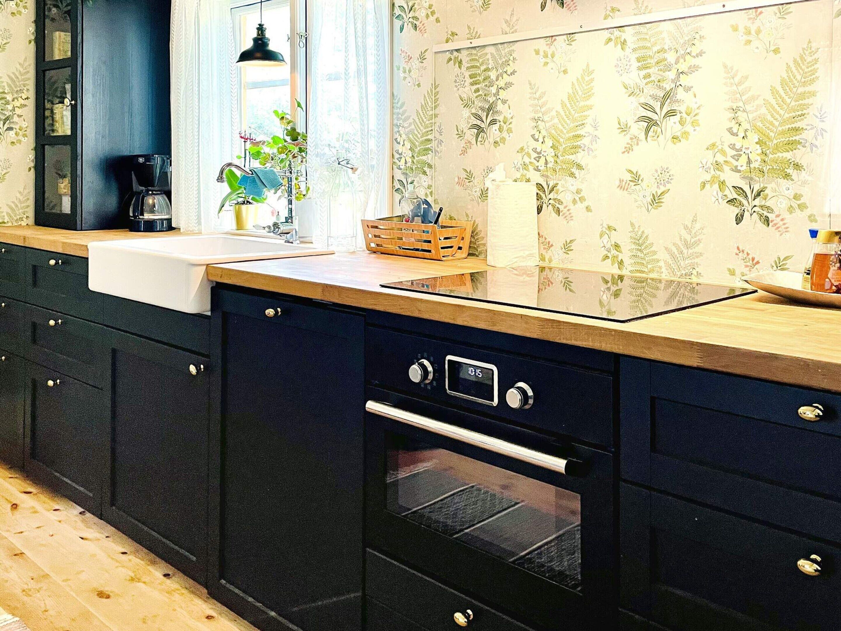 A kitchen with dark cabinets, a wooden countertop, a built-in oven, and a window with curtains.