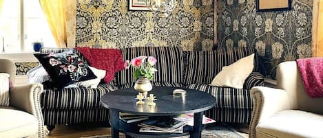 Un salon avec un canapé à rayures, une table basse ronde et un papier peint à motifs.