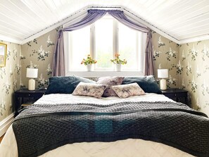 Een slaapkamer met een groot bed, twee nachtkastjes met lampen, een raam met gordijnen en bloemenbehang.