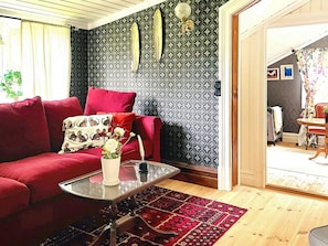 Un salon chaleureux avec un canapé rouge, une table basse en verre, un tapis à motifs et un mur agrémenté d’éléments décoratifs.