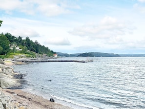 A coastal scene with a rocky shoreline, a pier extending into the water, and a distant hill with vegetation.
