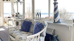 A wicker sofa with floral upholstery and blue cushions, a white lamp, a lighthouse model, and a view of a body of water through large windows. - 4 Star Holiday Home in Uddevalla (Uddevalla)