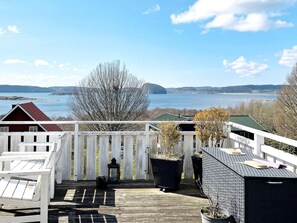 A wooden deck with a white railing, overlooking a body of water with distant landforms.
