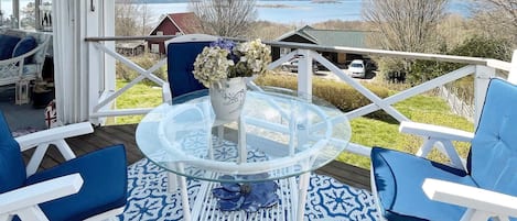 A deck with a glass table and chairs, a vase with flowers, and a view of a lake and buildings.