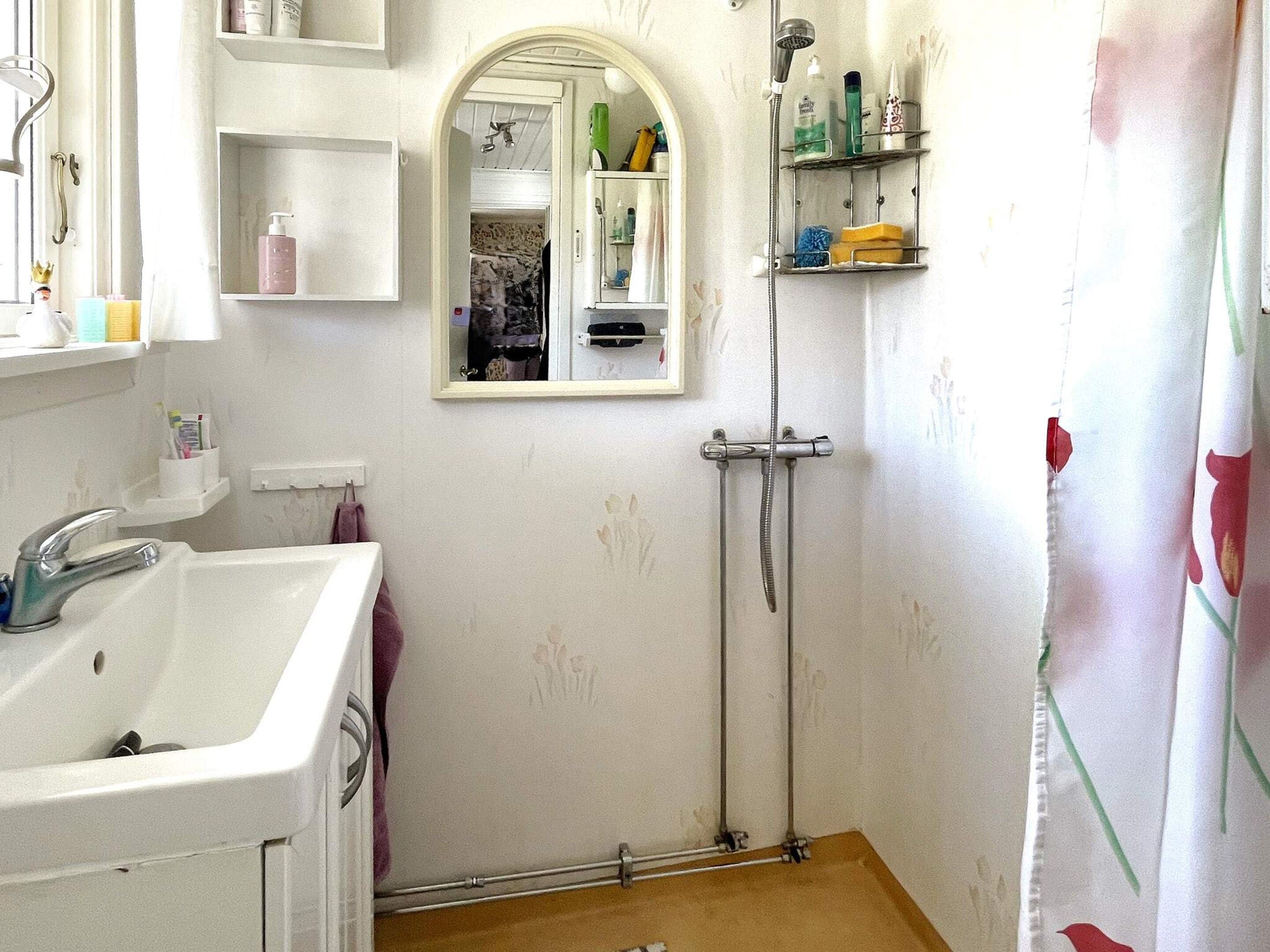Een badkamer met een wastafel, spiegel, douche en planken met toiletartikelen.